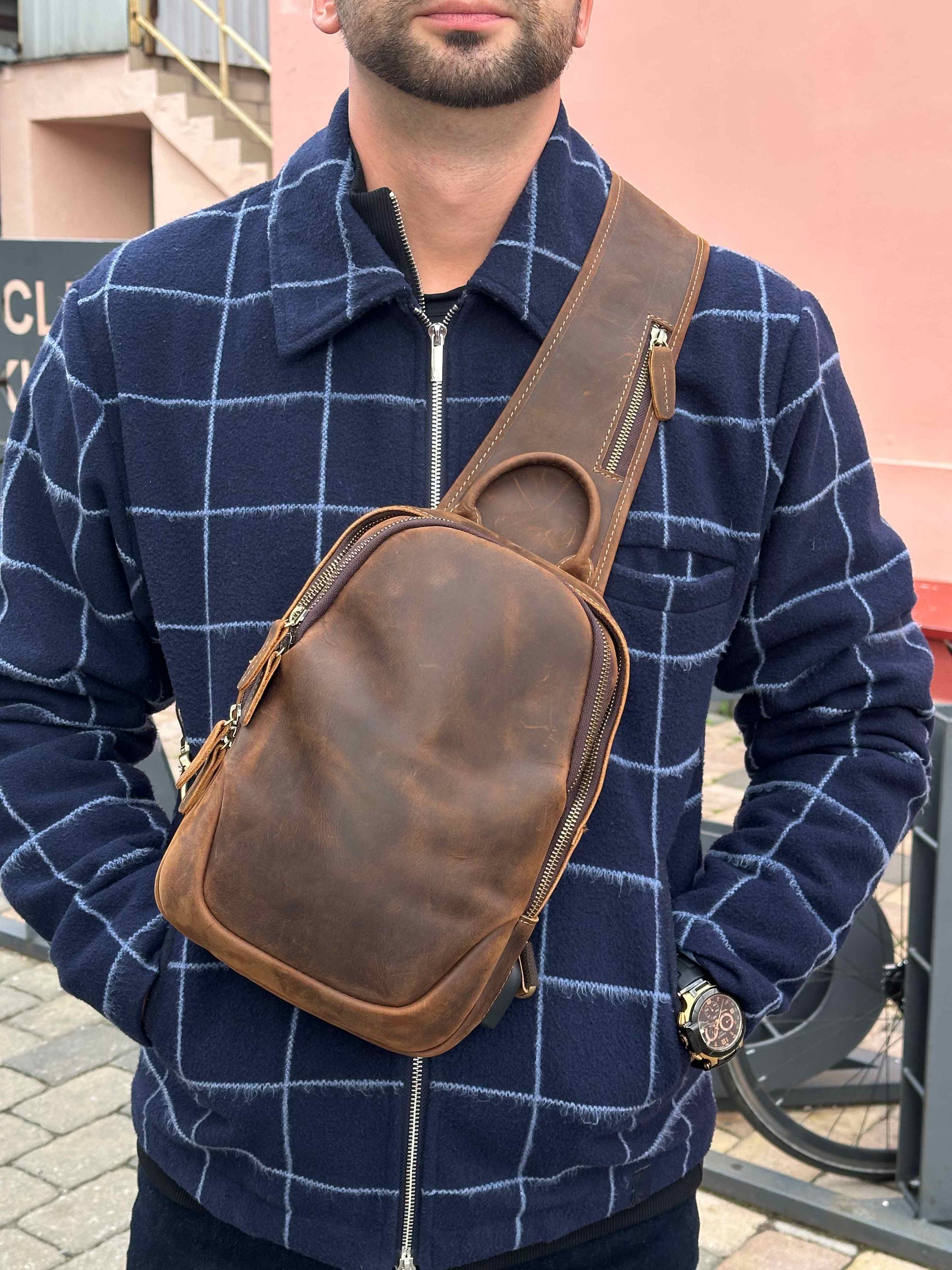 Men wearing a brown leather sling bag over his shoulder with a blue checkered sweater.