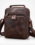 A dark brown distressed leather crossbody bag with multiple zippered compartments, a top handle, and an adjustable shoulder strap, shown on a light gray background.