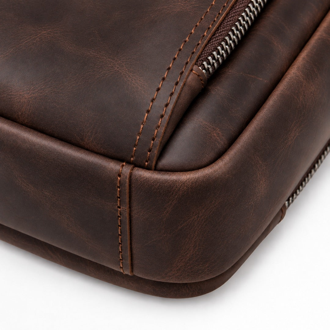 Close-up of a dark brown distressed leather bag corner showing stitched edges, rounded corners, and a metal zipper on a white background.