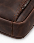 Close-up of a dark brown distressed leather bag corner showing stitched edges, rounded corners, and a metal zipper on a white background.