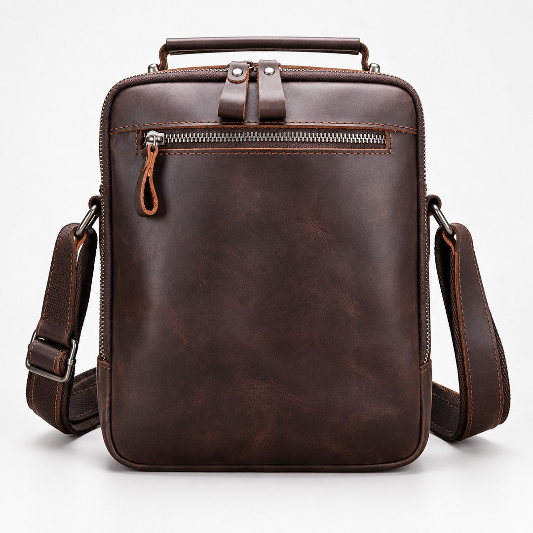 A dark brown leather crossbody bag with a top handle, front zippered pocket, and adjustable shoulder strap, shown on a clean white background.