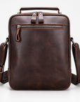 A dark brown leather crossbody bag with a top handle, front zippered pocket, and adjustable shoulder strap, shown on a clean white background.