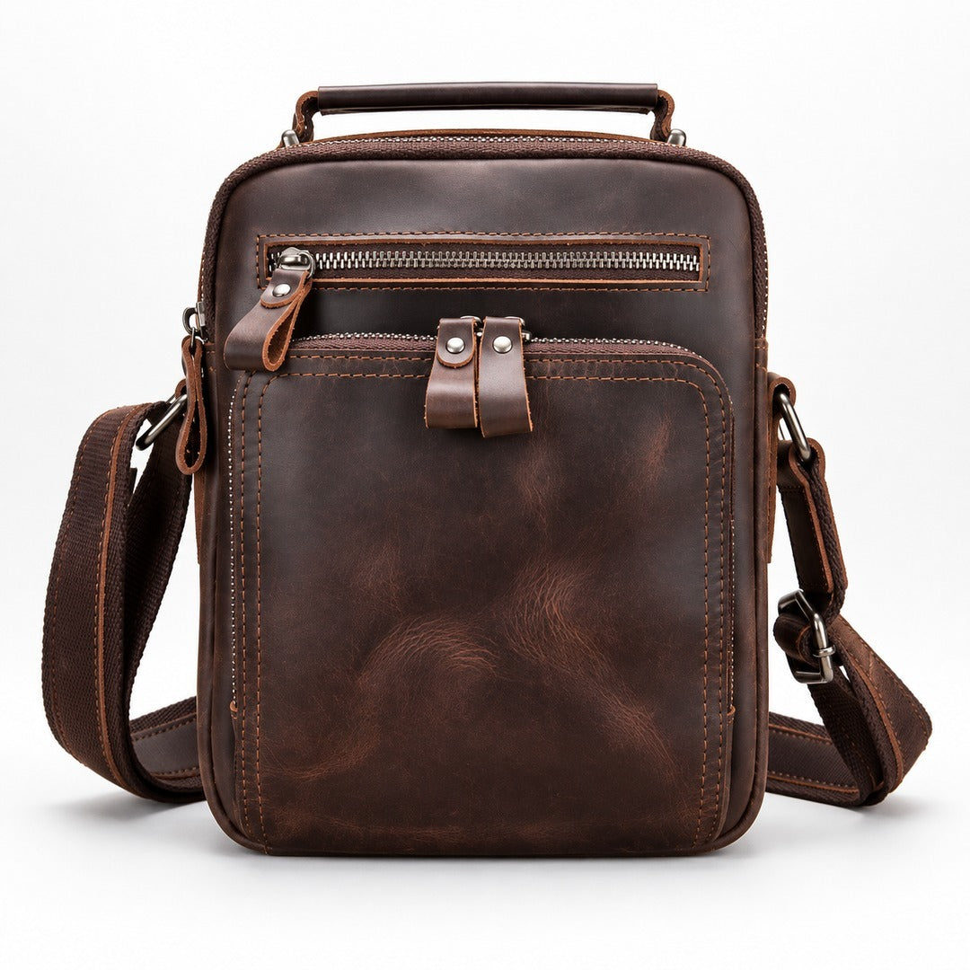 A dark brown distressed leather crossbody bag with a top handle, front zippered pocket, and adjustable shoulder strap, shown on a clean white background.