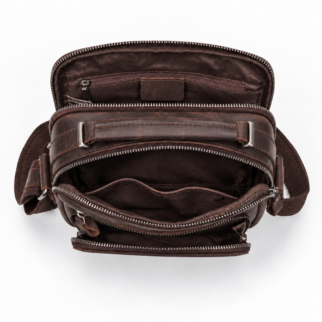 An overhead view of a dark brown leather crossbody bag shown open to display its interior compartments, pockets, and zipper details against a clean white background.