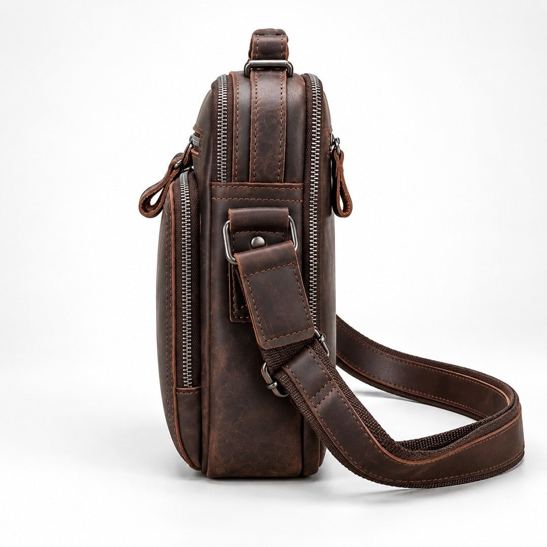 A dark brown distressed leather crossbody bag with multiple zippered compartments and an adjustable shoulder strap, shown from a side profile view on a white background.