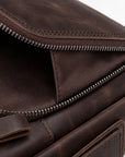 Close-up detail of a dark brown leather bag with an open zipper revealing a matching brown fabric interior, showing stitching and metal zipper teeth.