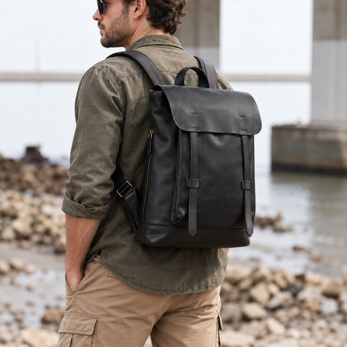 Minimalist black leather backpack for men with flap top, slim front straps, top handle and adjustable shoulder straps