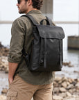Minimalist black leather backpack for men with flap top, slim front straps, top handle and adjustable shoulder straps
