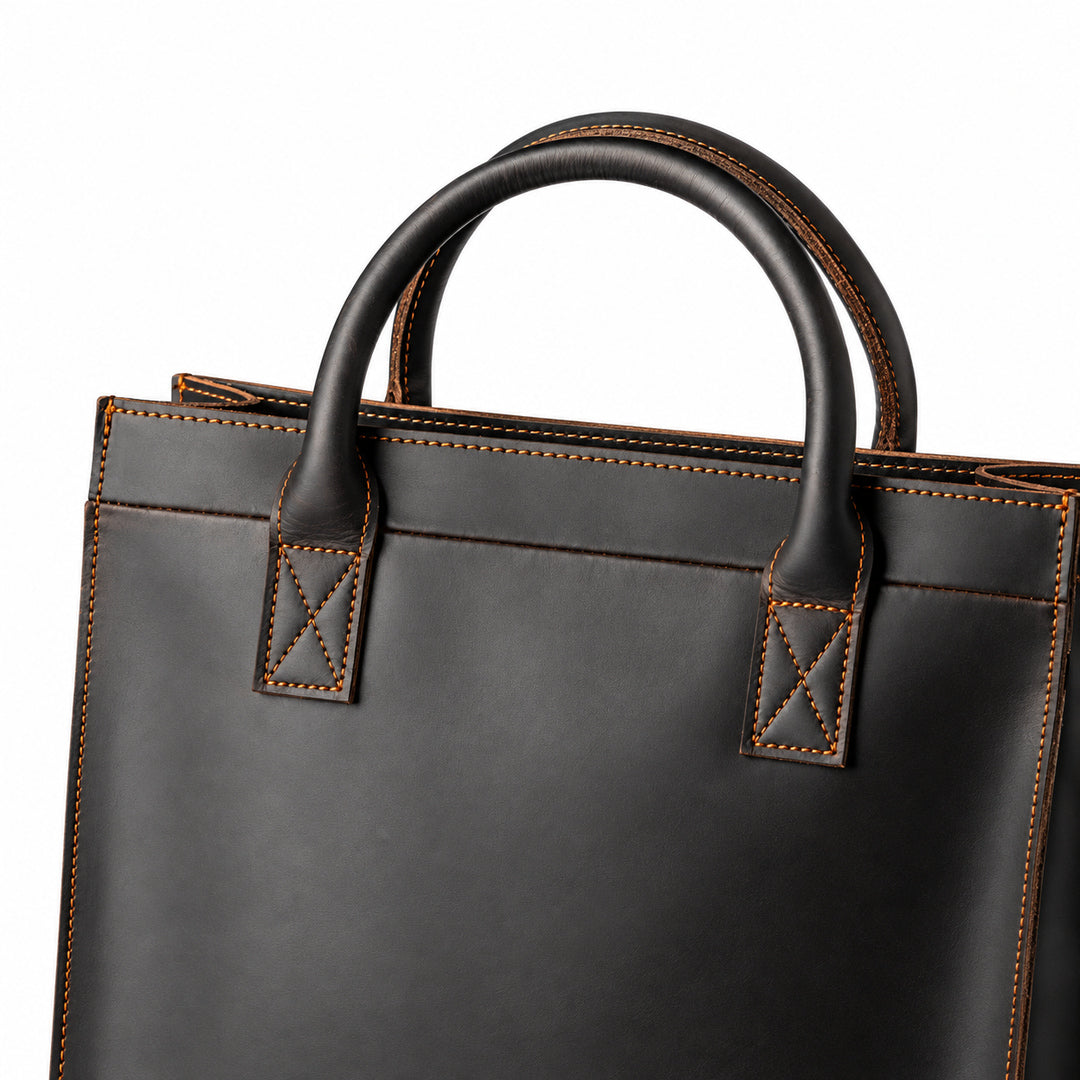 Minimalist black full-grain leather tote handle detail with cross stitching and rounded leather grips