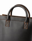 Minimalist black full-grain leather tote handle detail with cross stitching and rounded leather grips