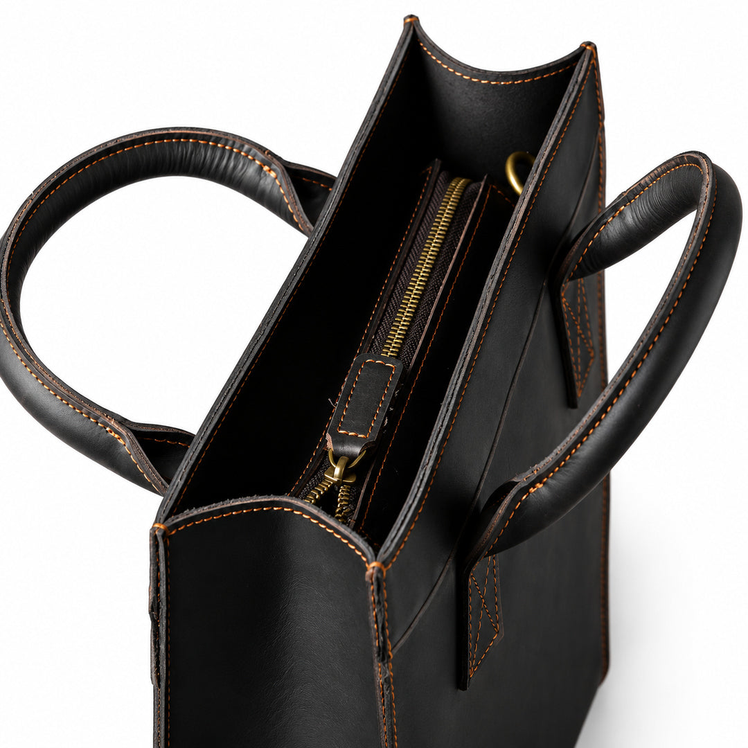 Minimalist black full-grain leather tote top view with a recessed zipper and leather pull