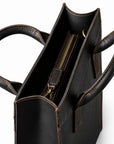 Minimalist black full-grain leather tote top view with a recessed zipper and leather pull