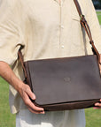 Model holding a dark brown leather satchel bag, showcasing its size and practicality