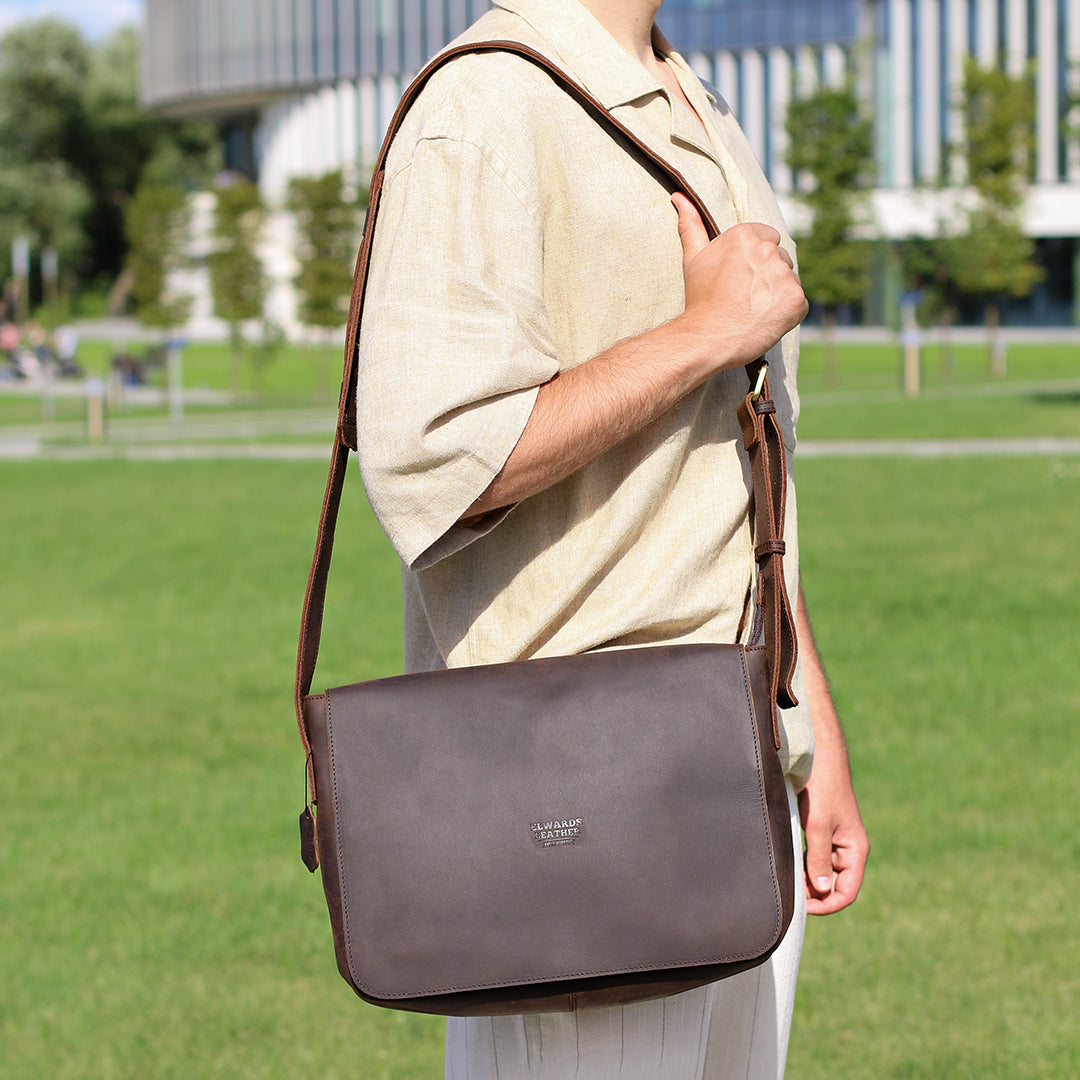 Model wearing a men&#39;s brown leather satchel bag in an outdoor urban setting