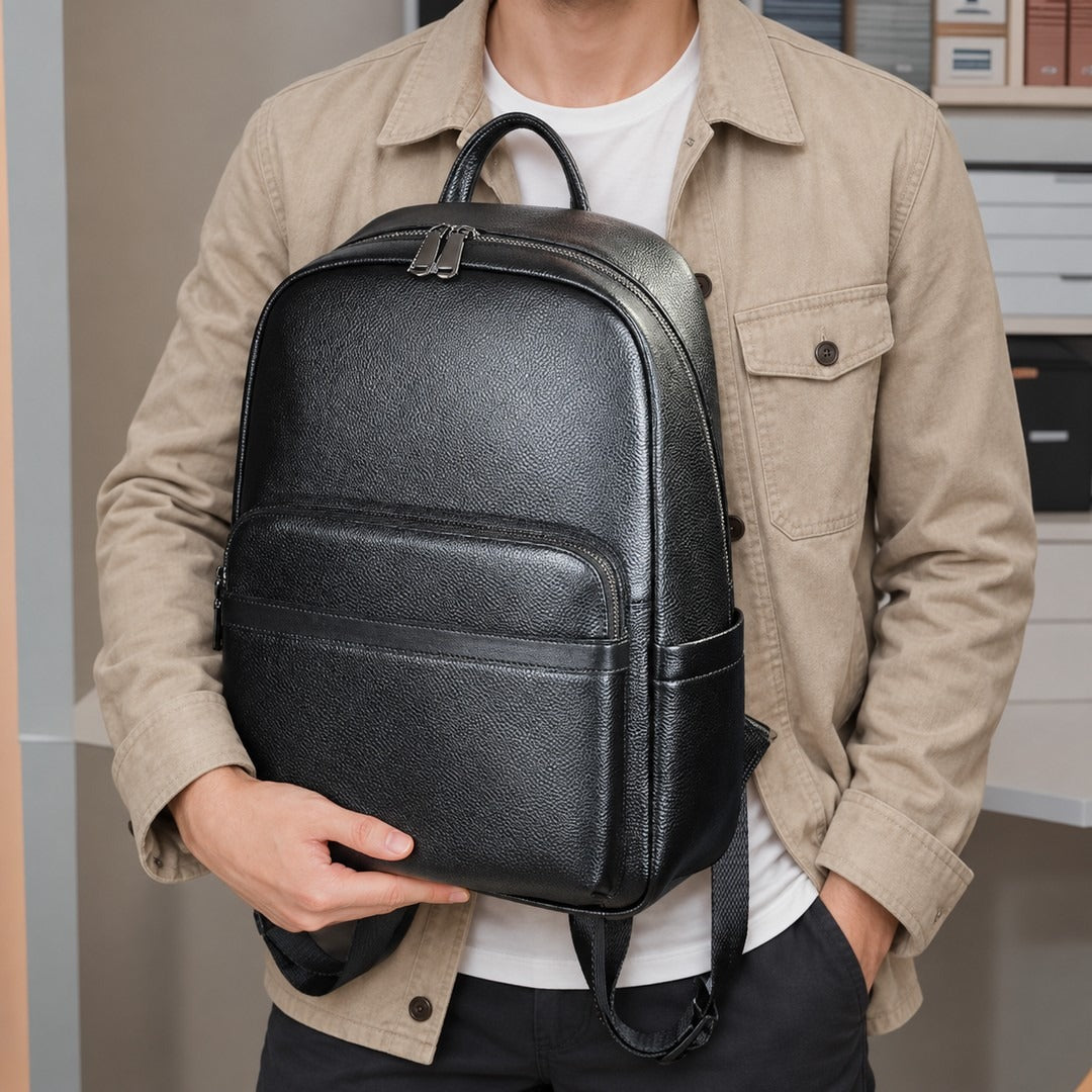 A man wearing a beige button-up shirt over a white t-shirt carries a black textured faux-leather backpack on his shoulder and holds it with one hand.