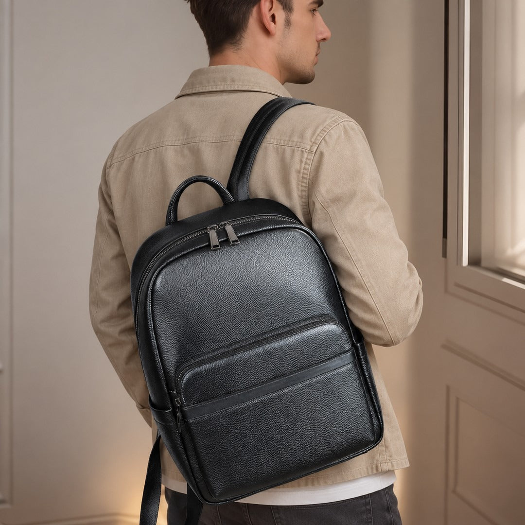 A man wearing a beige jacket is shown from the back, carrying a black textured leather backpack with top handles and dual zipper compartments.
