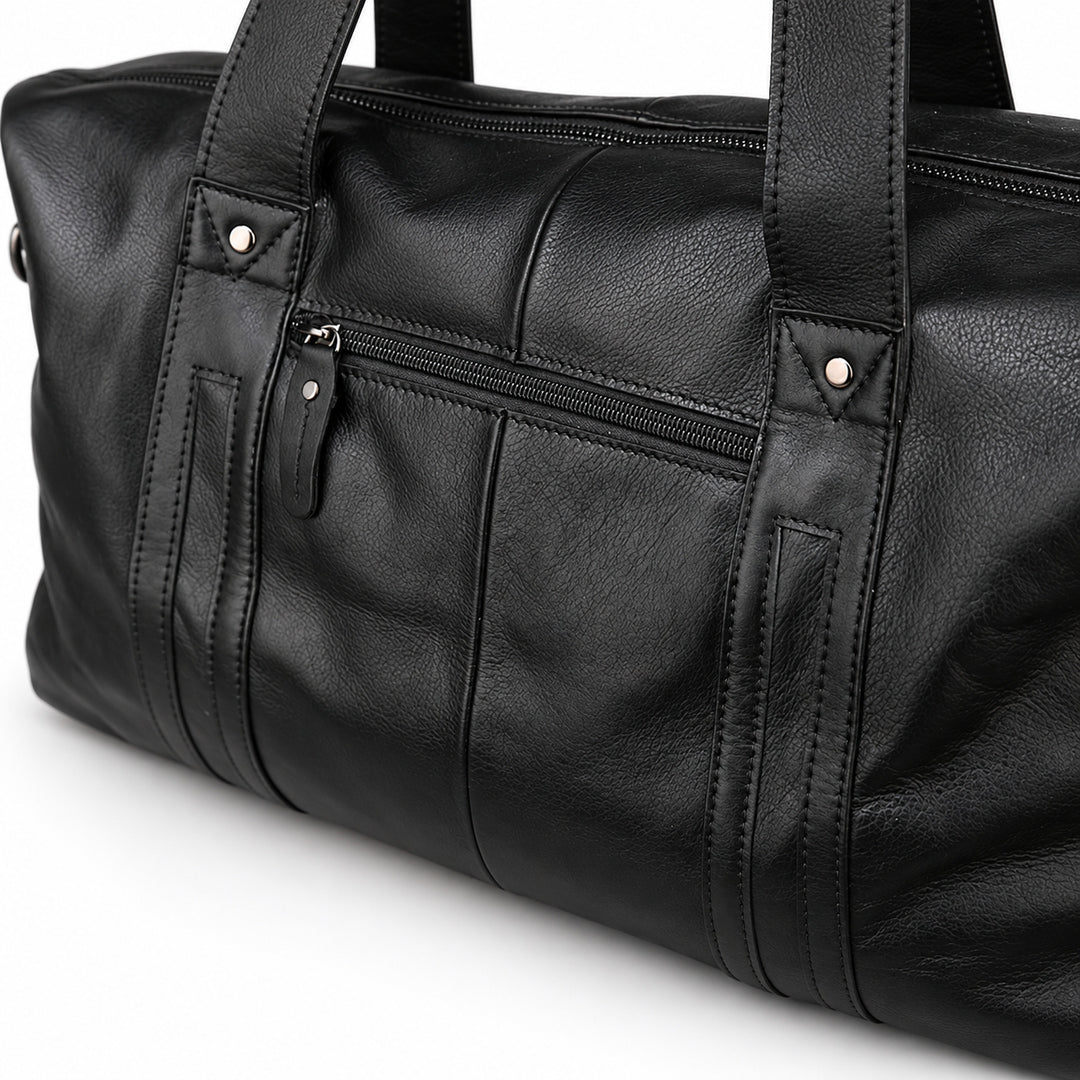 Modern black full-grain leather duffel bag detail showing the front zipper and riveted handle bands.