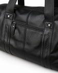 Modern black full-grain leather duffel bag detail showing the front zipper and riveted handle bands.