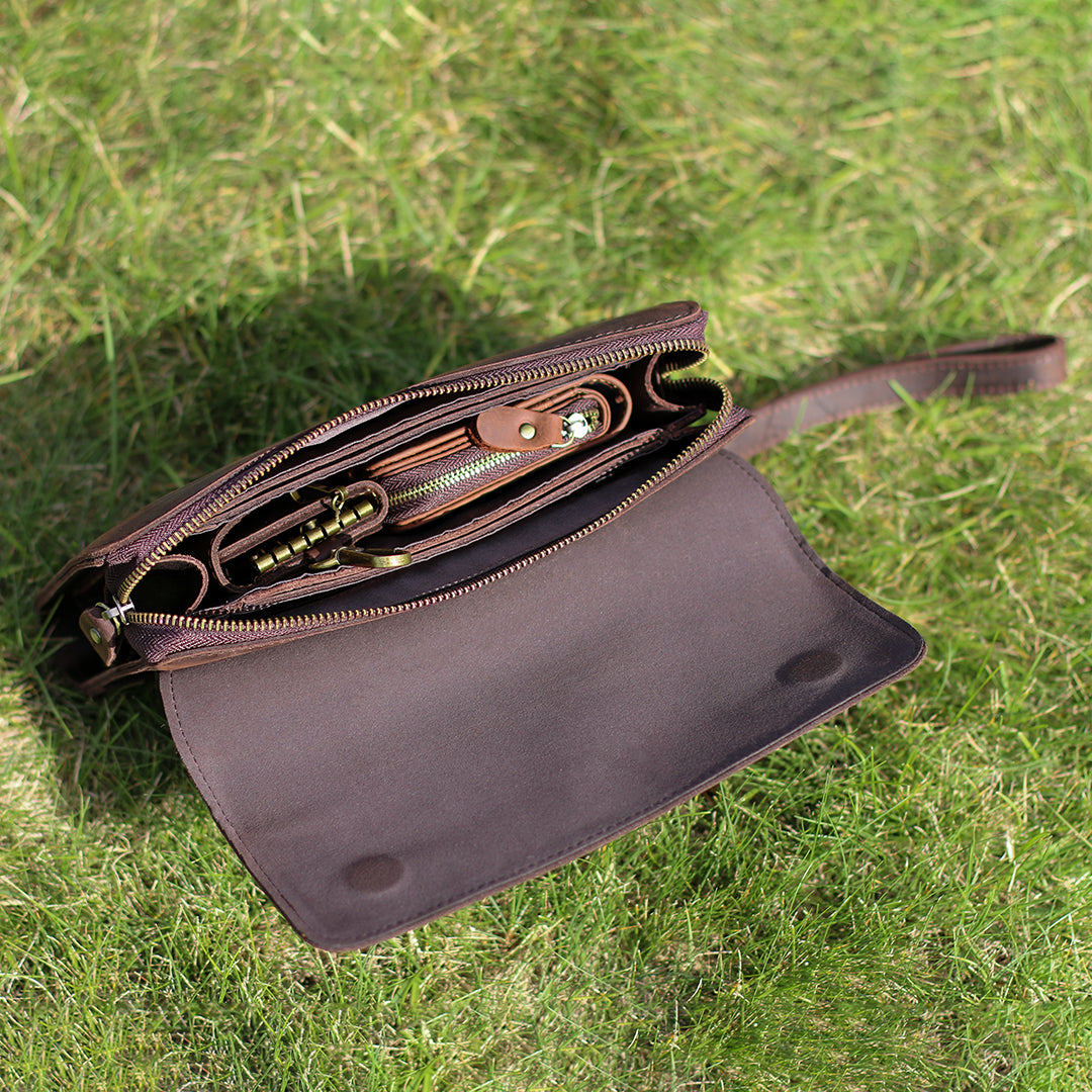 Top view of an open dark brown leather clutch on grass, showcasing its spacious and organized interior.