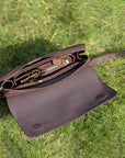 Top view of an open dark brown leather clutch on grass, showcasing its spacious and organized interior.