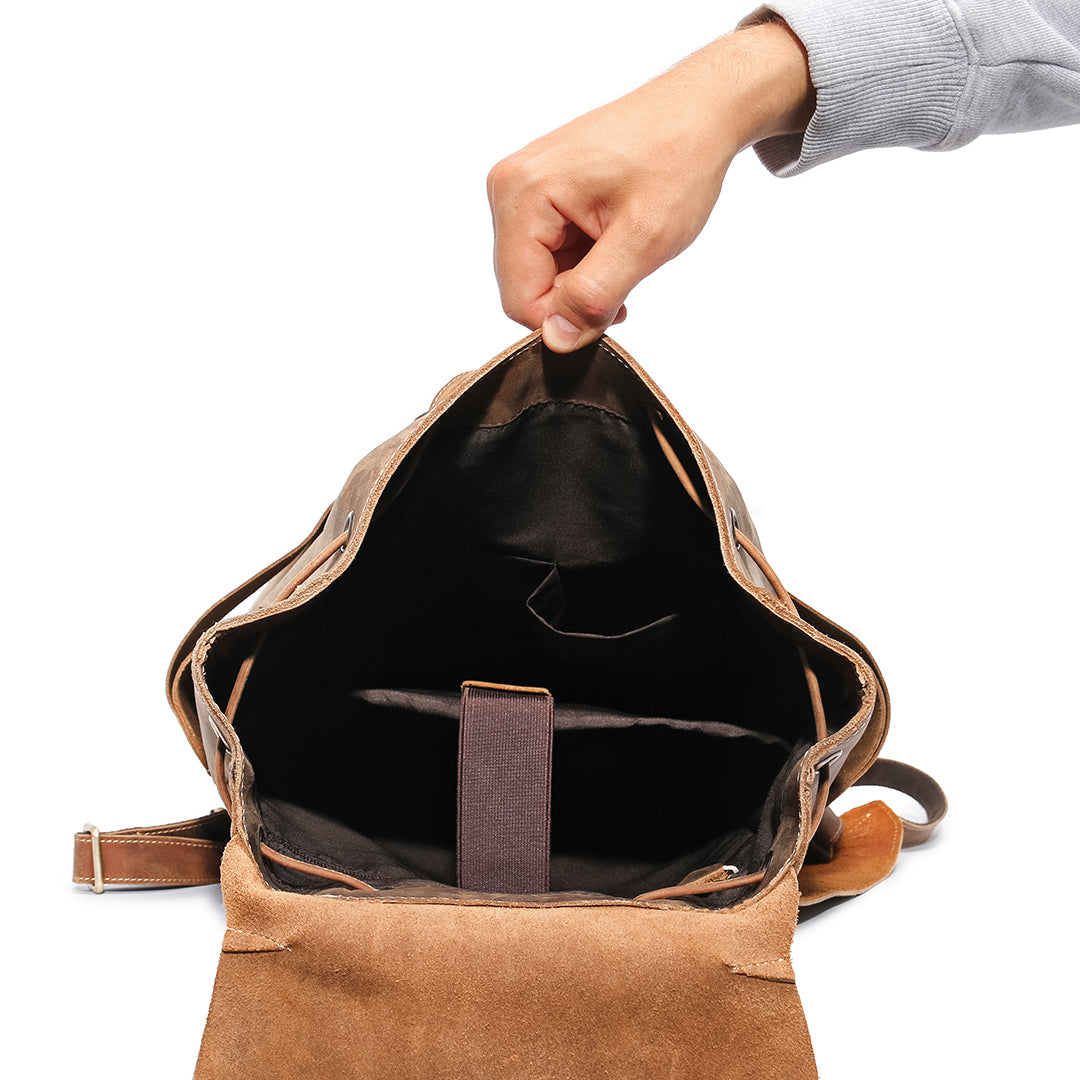 Interior view of a vintage brown leather backpack being held open, showing multiple compartments and padded laptop section