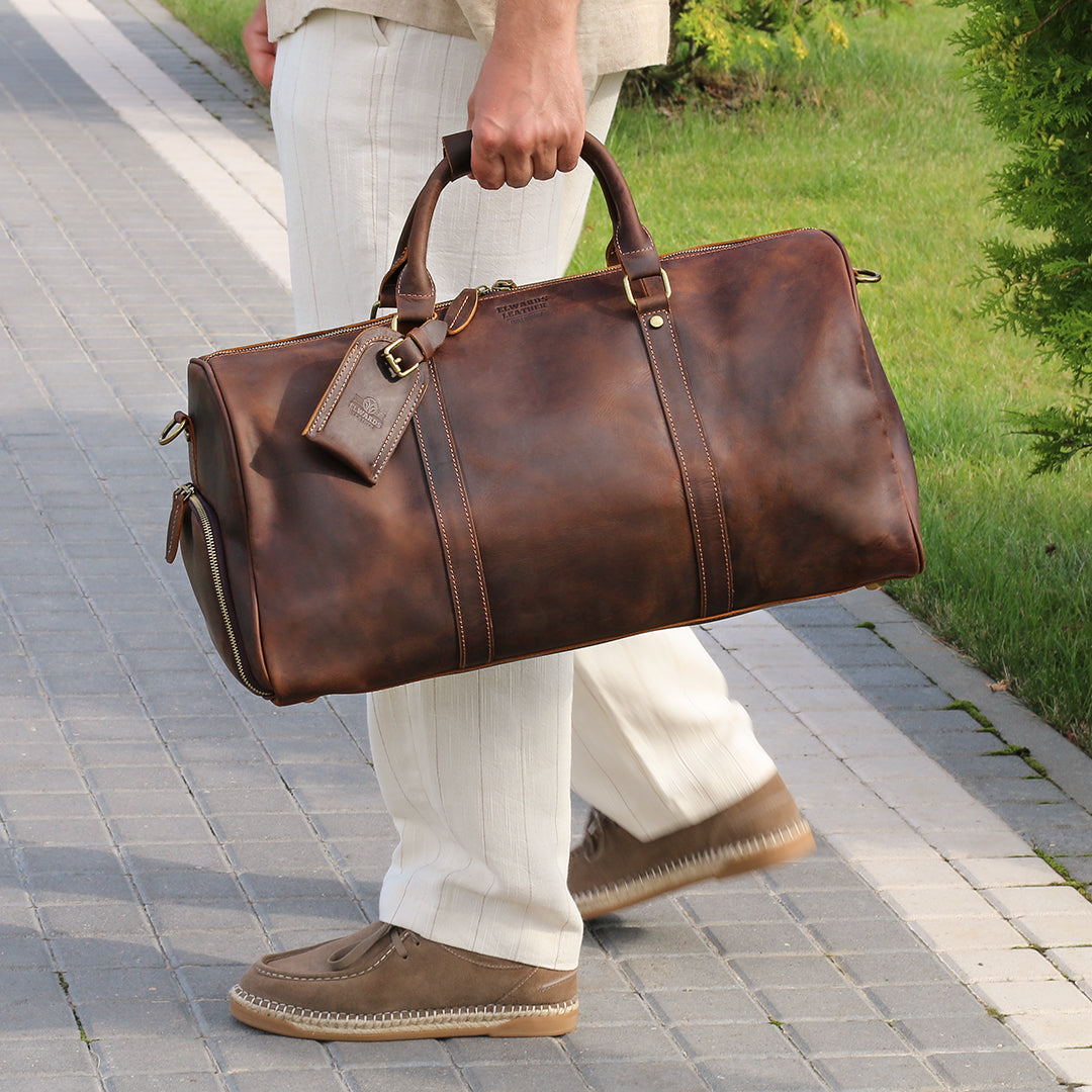 Premium brown leather duffle bag carried by hand on a sunny day, ideal for stylish travel.