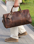 Premium brown leather duffle bag carried by hand on a sunny day, ideal for stylish travel.