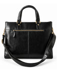 A black leather briefcase is shown from the back with a horizontal zip pocket, center seam and detachable shoulder strap.