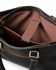 The black leather briefcase interior shows a wide brown sleeve with a retaining strap and black leather end tab.