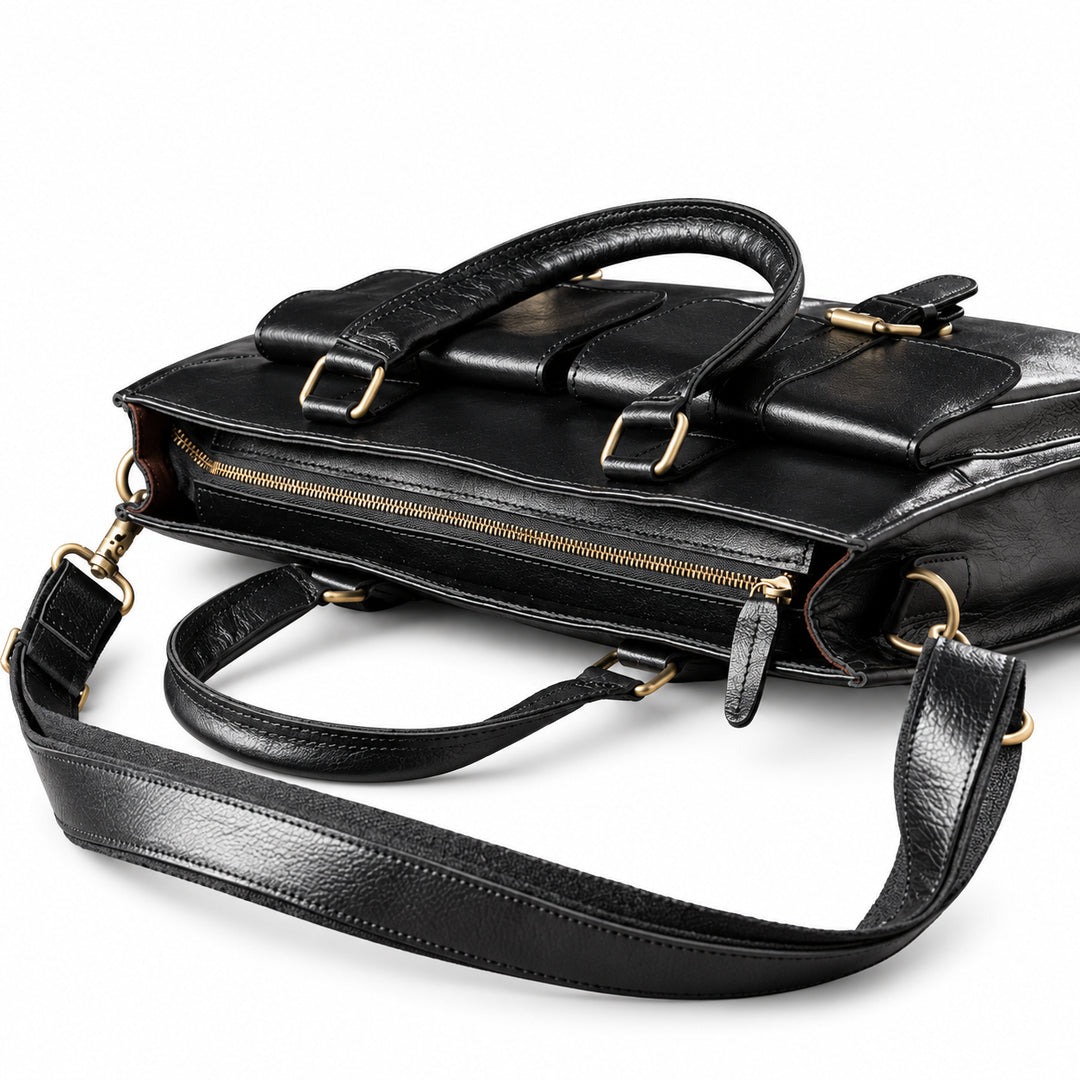 A black leather briefcase lies flat to show its brass-tone top zipper, leather pull and folded carry handles.