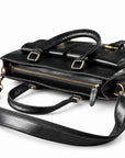 A black leather briefcase lies flat to show its brass-tone top zipper, leather pull and folded carry handles.