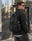 Quilted black leather backpack for men with flap top, buckle straps, drawstring closure and multiple exterior zip pockets