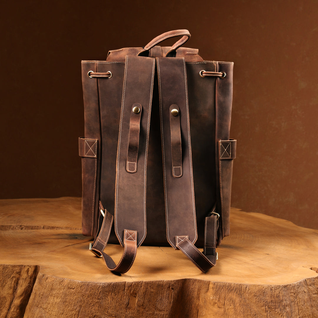 Full rear view of a brown leather backpack standing upright on a rustic wooden table