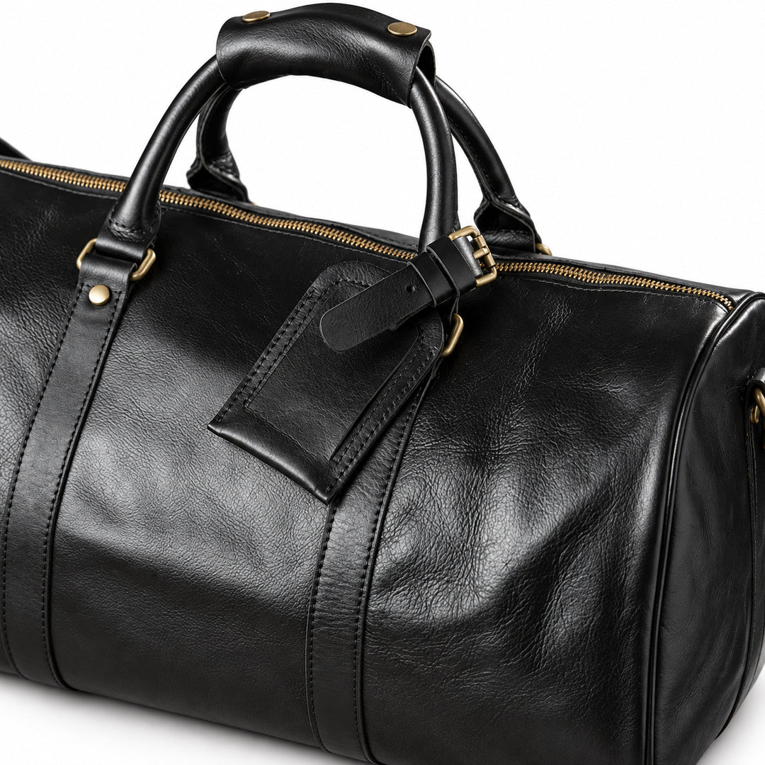 Refined black full-grain leather duffel bag with a buckled leather luggage tag