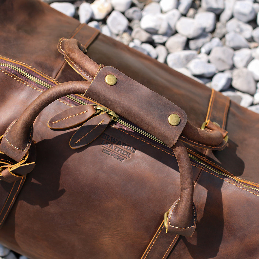 Close-up of reinforced leather handles and brass hardware on a vintage-inspired duffle bag.