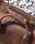 Close-up of reinforced leather handles and brass hardware on a vintage-inspired duffle bag.