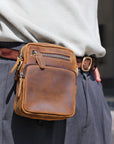 Brown leather waist bag worn by a person with a blurred background