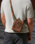 Person wearing a brown leather crossbody bag on a city street.
