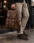 Rugged brown leather backpack for men with multiple exterior pockets, buckle closures and adjustable shoulder straps
