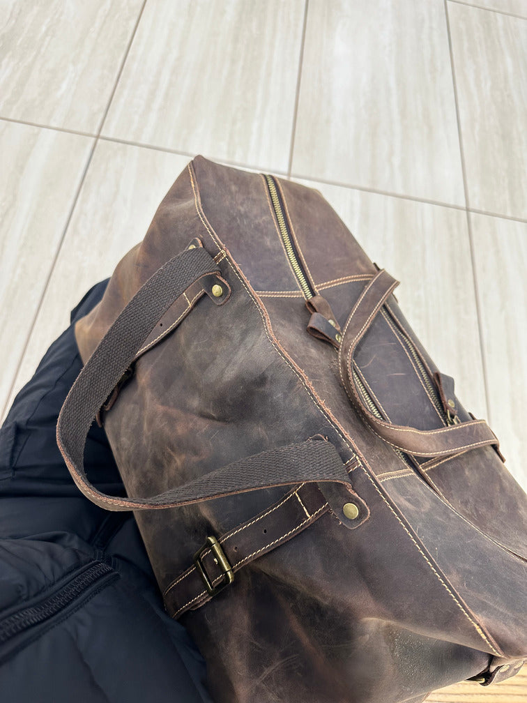 Side view of brown leather duffle bag, featuring adjustable straps, perfect for rugged travel and business trips
