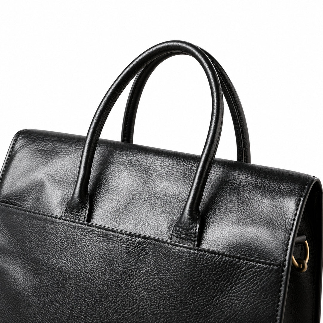 A close-up of the black full-grain leather briefcase shows rolled handles, stitched leather bases and the upper pocket edge.