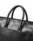 A close-up of the black full-grain leather briefcase shows rolled handles, stitched leather bases and the upper pocket edge.