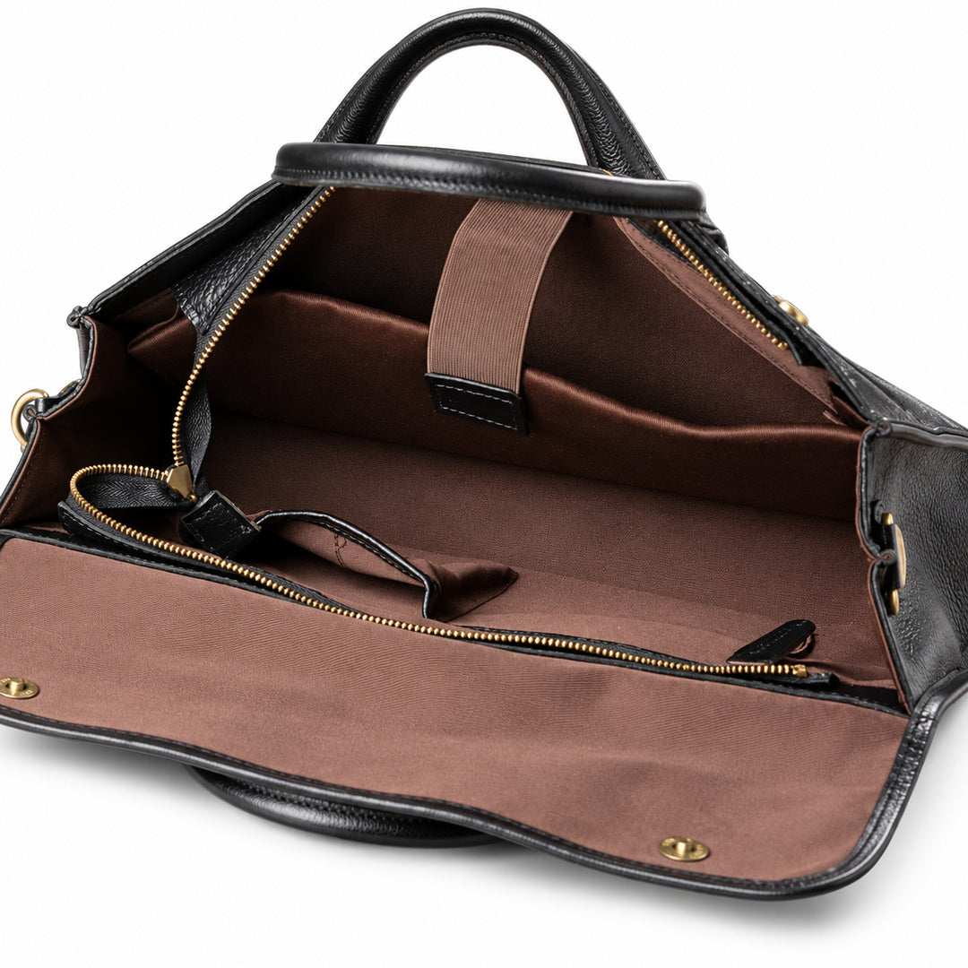 The open black full-grain leather briefcase reveals a brown sleeve with a retaining strap and a black leather end tab.