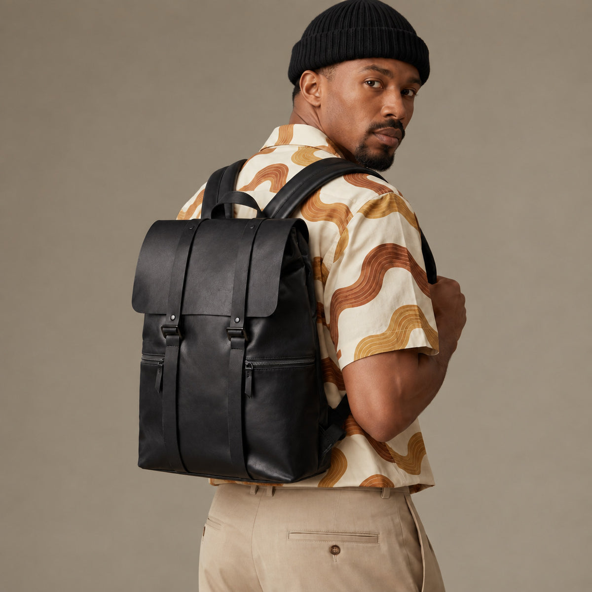 Sleek black leather backpack for men with flap top, vertical strap details and front zip pockets, worn as an urban everyday bag