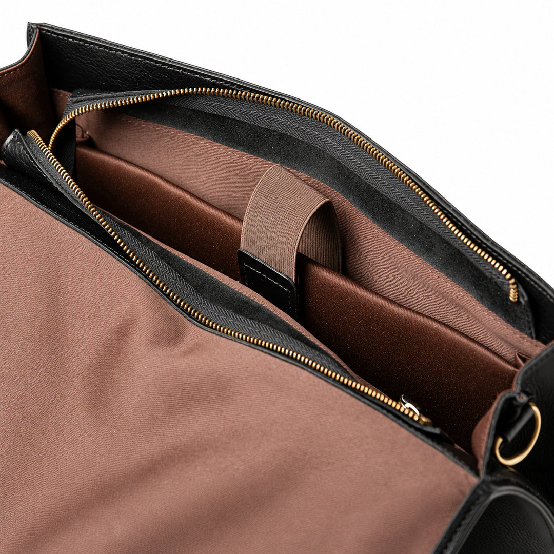 The open black full-grain leather briefcase reveals a brown sleeve with a retaining strap and a black leather end tab.