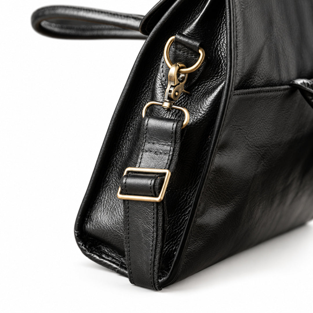 A close-up of the black full-grain leather briefcase shows the brass-tone swivel clasp, D-ring and stitched strap attachment.