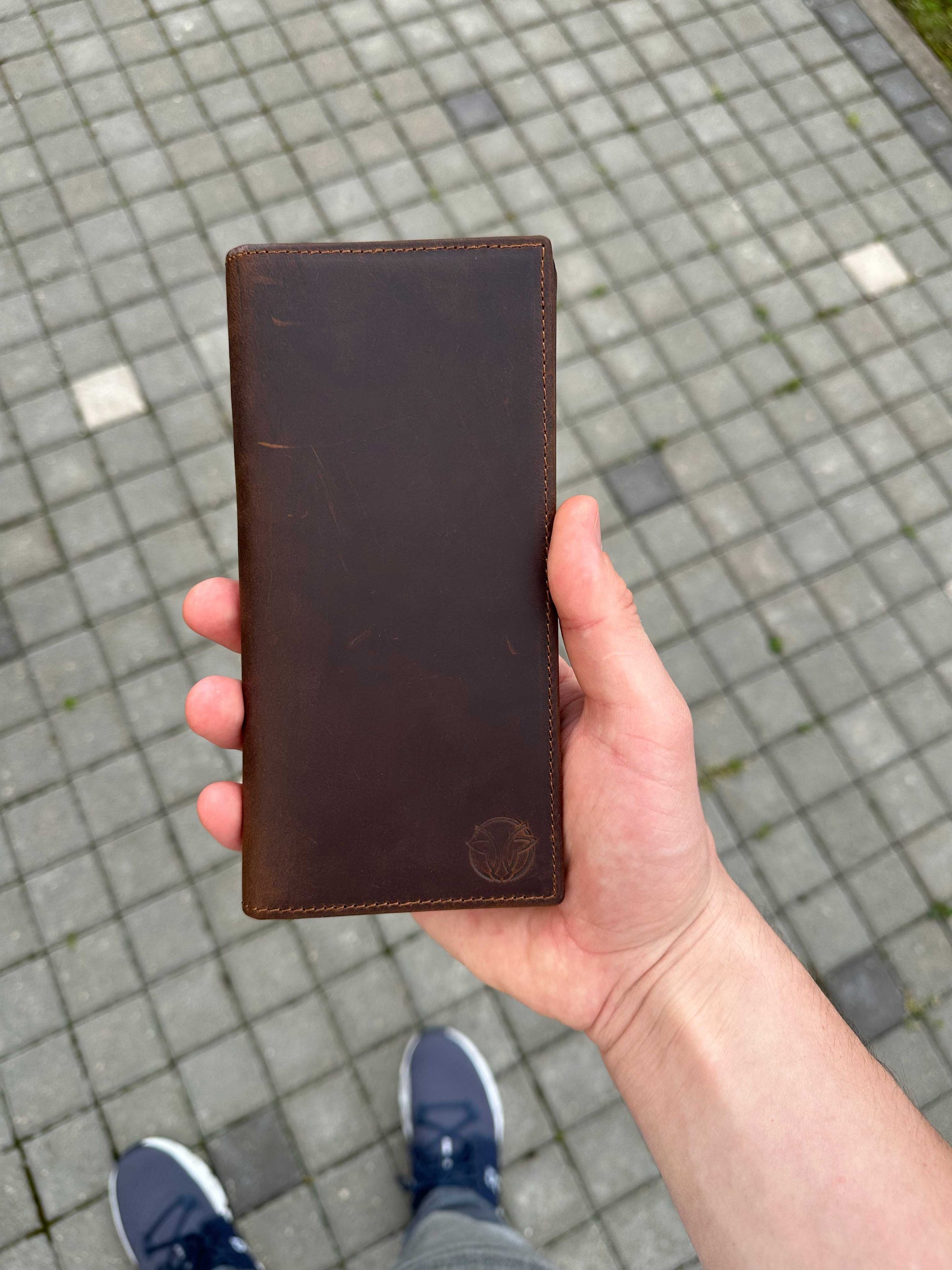 Hand holding a brown leather wallet on a paved ground
