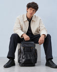 Spacious black leather travel backpack for men with buckle flap, multiple exterior pockets, top handle and adjustable shoulder straps