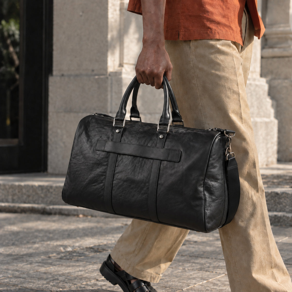 Spacious black leather duffle bag for men with dual top handles, adjustable shoulder strap, side zip pocket and large weekender design