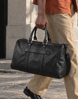 Spacious black leather duffle bag for men with dual top handles, adjustable shoulder strap, side zip pocket and large weekender design